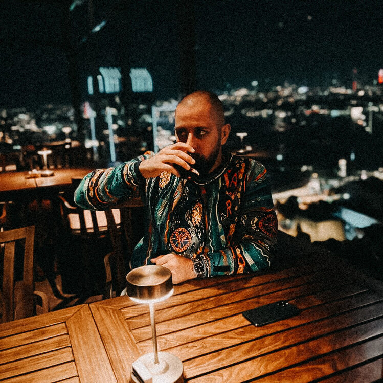 Isa Ulubaev trinkt Kaffee in einer Location mit einer Skyline im Hintergrund